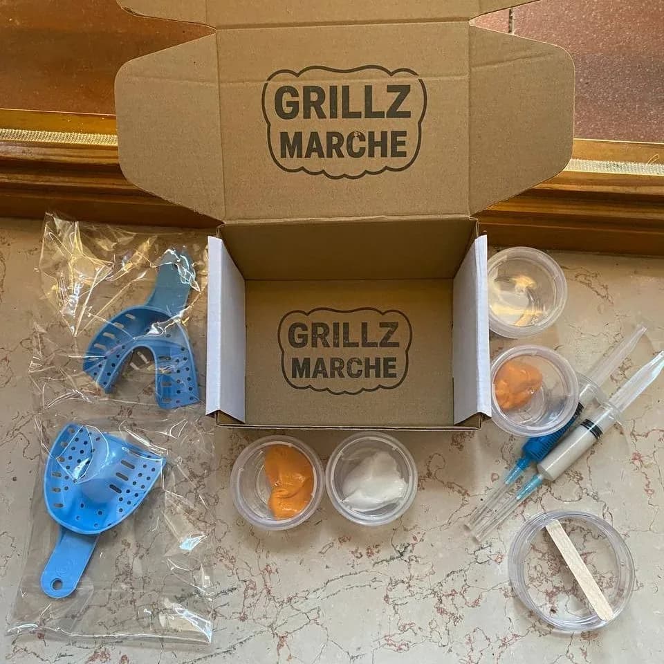 Kit impronta Grillz Marche aperto: scatola timbrata col logo, due vaschette blu per arcata superiore e inferiore, quattro barattolini di pasta pre-dosata, due siringhe di pasta fluida e vassoietto col bastoncino per miscelare