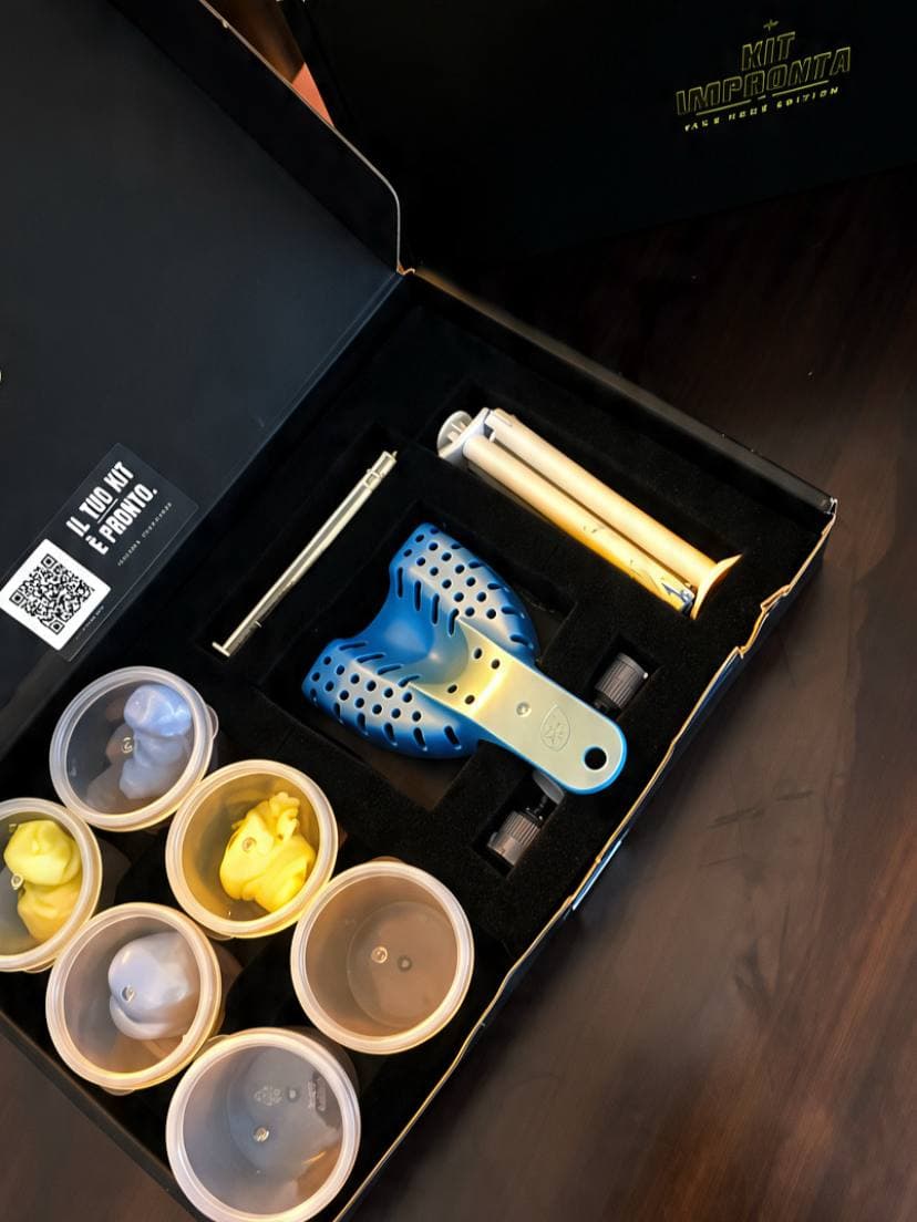 Il kit impronta aperto di tre quarti: coperchio col logo e la scritta Kit Impronta Take Home Edition, barattolini di pasta pre-dosata, porta-impronte blu, siringa a doppia camera e puntali